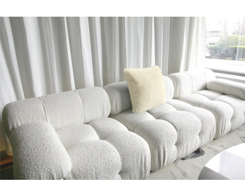 Modulsoffa med kudde och vadderad struktur framför ett fönster med gardin