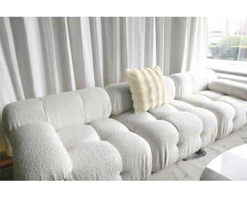 Stor soffa med mjuk kudde framför ett fönster med gardiner