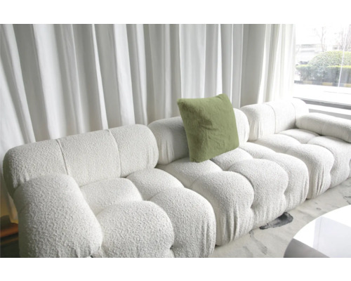 Vit modulsoffa med kudde och strukturöverdrag framför ett fönster med gardiner