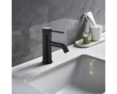 Svart tvättställsblandare bredvid vitt handfat och badrumsartiklar