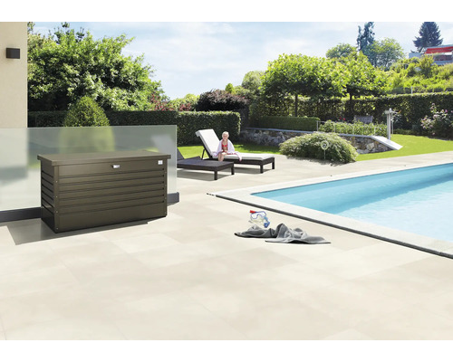 Utomhusscen med en förvaringslåda bredvid en pool, solstolar och en trädgård.