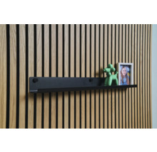 Svart vägghylla framför en träpanelvägg med dekoration