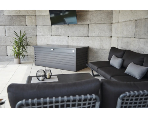 Utomhusområde med en grå förvaringslåda, en soffa, ett bord och en växt.