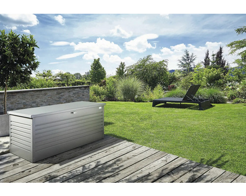 Trädgårdslandskap med en förvaringslåda i metall och en solstol på en gräsmatta