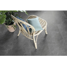 Scen med en rottingstol med kuddar och en krukväxt på ett grått golv.