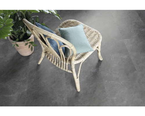 Scen med en rottingstol med kuddar och en krukväxt på ett grått golv.