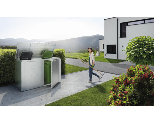 Soptunnebox av metall med två soptunnor och en kvinna med en kratta i trädgården