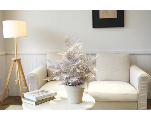 Dekorativ konstgjord ormbunke i kruka på ett bord framför en soffa