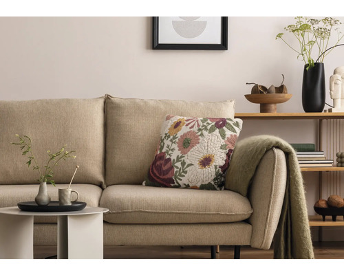 Vardagsrumsscen med beige soffa, blommönstrad prydnadskudde och sidobord