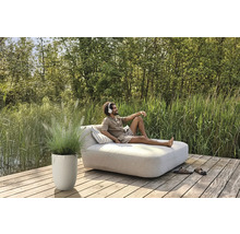 Man kopplar av på en trädgårdssäng med hörlurar, bredvid honom en blomkruka med prydnadsgräs på en träterrass.