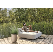 Scen med man på en trädgårdsbänk med kuddar, krukväxt och skor på en träterrass vid en sjö