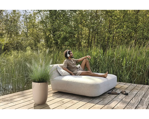 Scen med man på en trädgårdsbänk med kuddar, krukväxt och skor på en träterrass vid en sjö