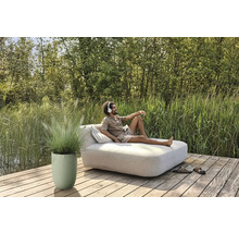 Man kopplar av med hörlurar på en trädgårdsbänk på en träterrass bredvid en planteringslåda med prydnadsgräs.