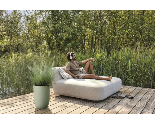 Man kopplar av med hörlurar på en trädgårdsbänk på en träterrass bredvid en planteringslåda med prydnadsgräs.