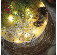 Dekoration med silverpärlband, grangrenar och tallkottar på ett runt bord.