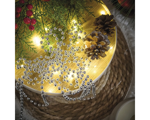 Dekoration med silverpärlband, grangrenar och tallkottar på ett runt bord.