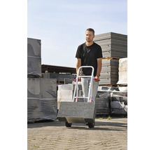 Man transporterar gatstenar med en säckvagn utomhus.