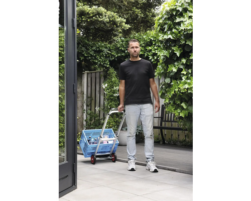 Man transporterar en blå shoppingbox med en vagn i trädgården