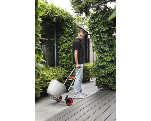 Man transporterar blomkruka med en skottkärra i trädgården.