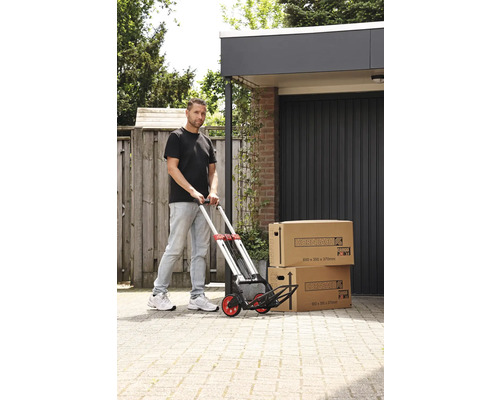 Man skjuter en kärra med två flyttkartonger framför ett garage.
