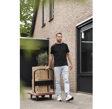 Man transporterar flyttkartonger med en transportvagn framför ett hus.