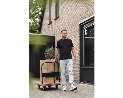 Man transporterar flyttkartonger med en transportvagn framför ett hus.