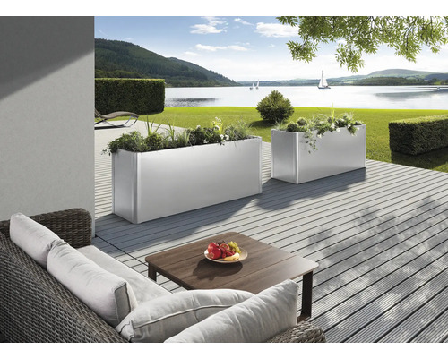 Scen med två rektangulära, silverfärgade planteringslådor på en terrass med utsikt över en sjö