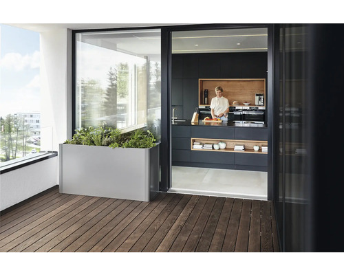 Scen med en blomlåda på en träbalkong och en kvinna som står i ett kök