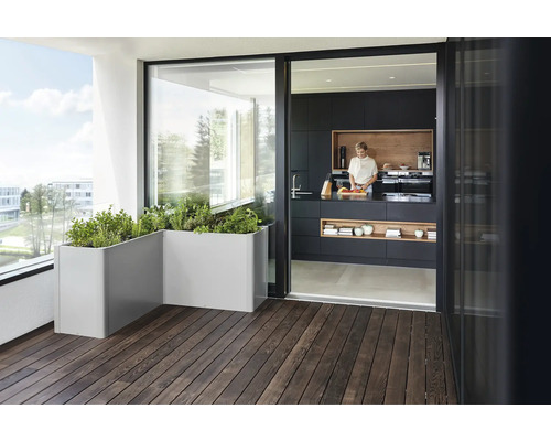 Modernt designad terrass med trägolv, planteringslådor och öppen passage till köket