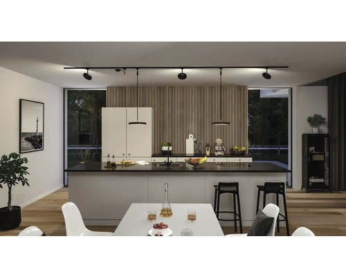 Ljust kök med köksö, svarta barstolar och skenspotlights i taket.