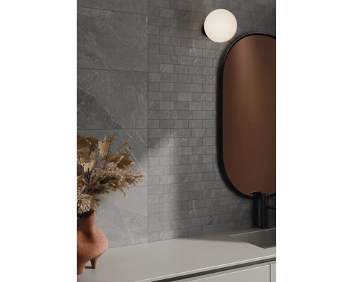 Badrum med grå väggplattor i stenlook, spegel och lampa