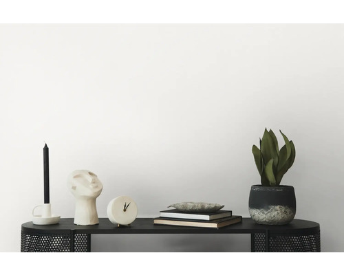 Dekorativ scen på en svart hylla med ljus, huvudskulptur, klocka, böcker och krukväxt.