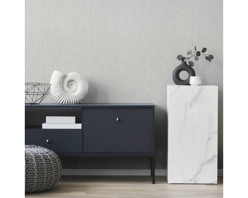 Inredningsscen med byrå, sidobord och dekoration mot en tapet med subtil struktur.