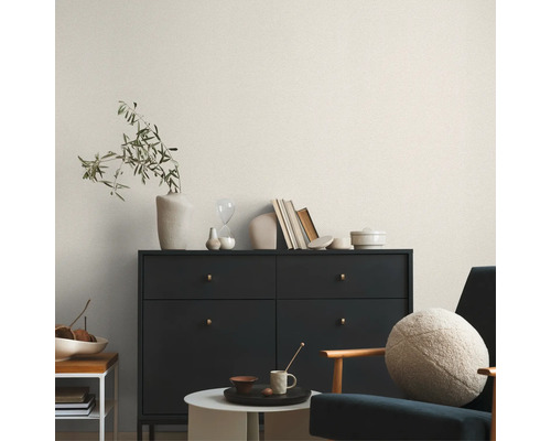 Vardagsrum med byrå, stol och dekorativa föremål framför en ljusmönstrad tapet