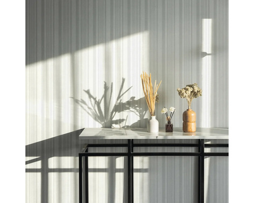 Dekorativa torkade blommor i vaser på ett bord framför en randig vägg.