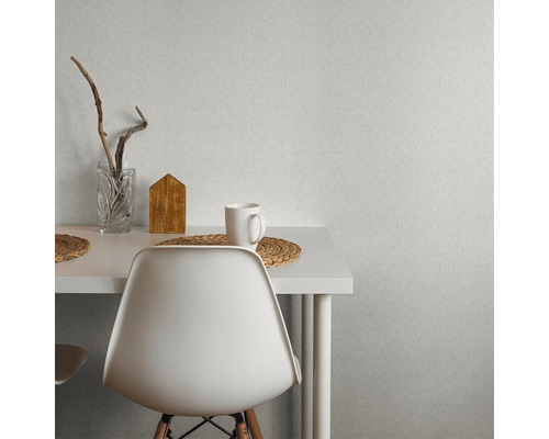 Miljöbild med strukturtapet på väggen, ett bord, en stol, ett glas, ett trähus och en kopp