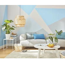 Vardagsrum med soffa, bord, lampa och krukväxter framför en vägg med geometriska mönster