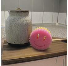 Keramikburk med lock och en diskssvamp med smiley-ansikte på en träbräda