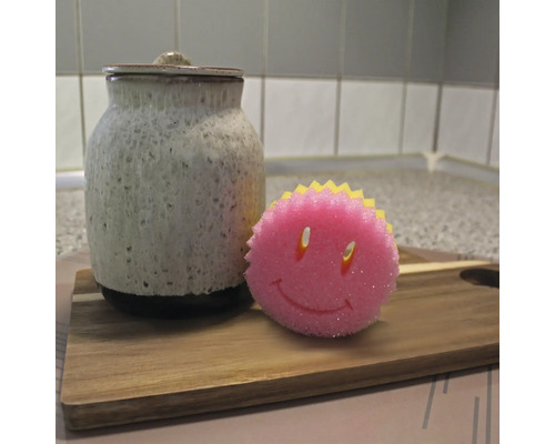 Keramikburk med lock och en diskssvamp med smiley-ansikte på en träbräda