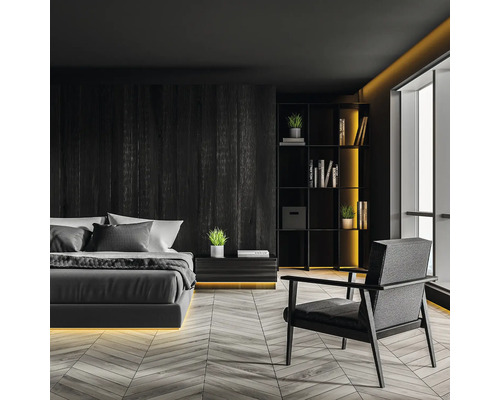 Sovrum med säng, sängbord, bokhylla och fåtölj i mörk design