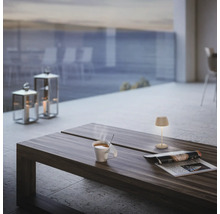 Scen med ett soffbord på en terrass, med en kopp, en tidning och en lampa på den, lyktor i bakgrunden.