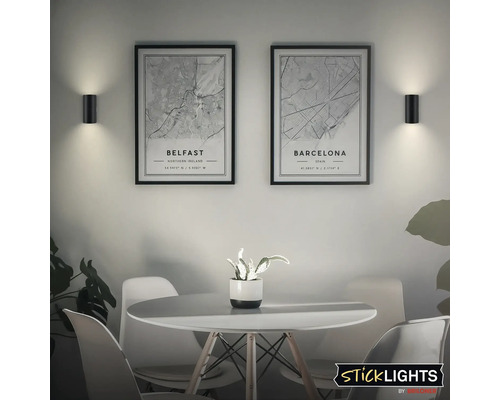 Scen med två vägglampor och dekorativa bilder ovanför ett bord.