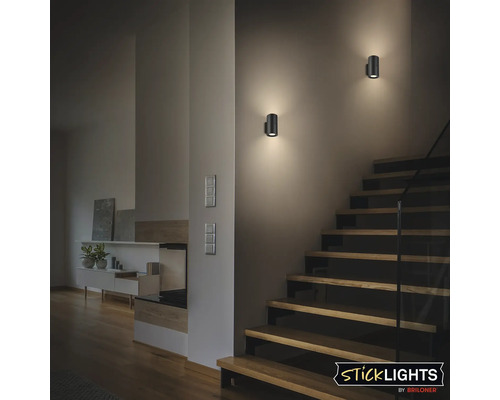 Två svarta vägglampor bredvid en trätrappa inomhus.