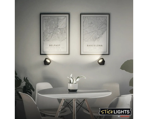 Vardagsrum med bord, stolar, vägglampor och inramade stadskartor över Belfast och Barcelona