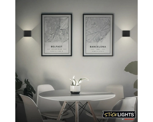 Vardagsrum med två vägglampor och dekorativa stadskartor ovanför ett matbord.