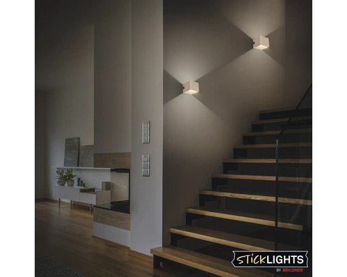 Vardagsrum med trappa och två kubformade vägglampor.