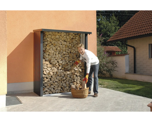 Person fyller vedkorg vid en vedbod