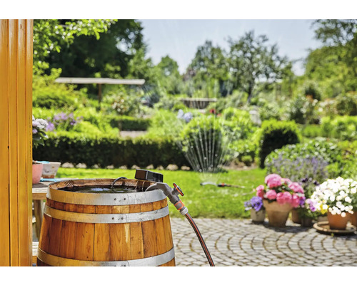 Trätunna som regnvattentunna med kran och trädgårdsslang i trädgården