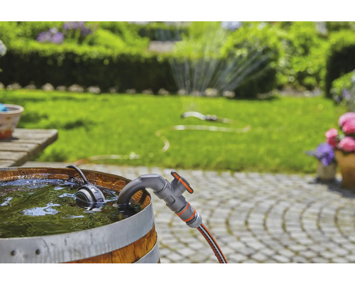 Trädgårdsscen med regntunna, kran och trädgårdsslang framför grön gräsmatta