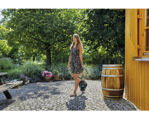 En kvinna bär en dränkbar tryckpump i en trädgård med träd och blommor